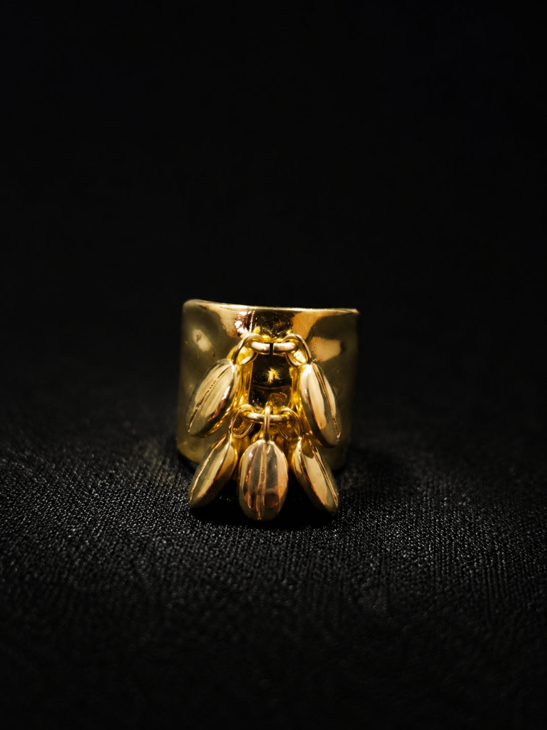 A gold ring featuring a sculpted bee design on a wide band, photographed against a dark textured background.