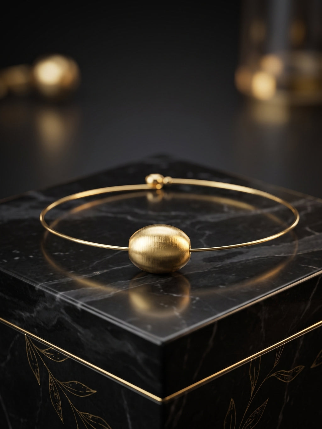 A gold-plated bangle bracelet with a textured spherical bead, displayed on a black marble block.