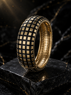 A wide gold ring with a black grid pattern on the exterior and a matching gold interior, displayed on a dark stone surface against a dark marble background.