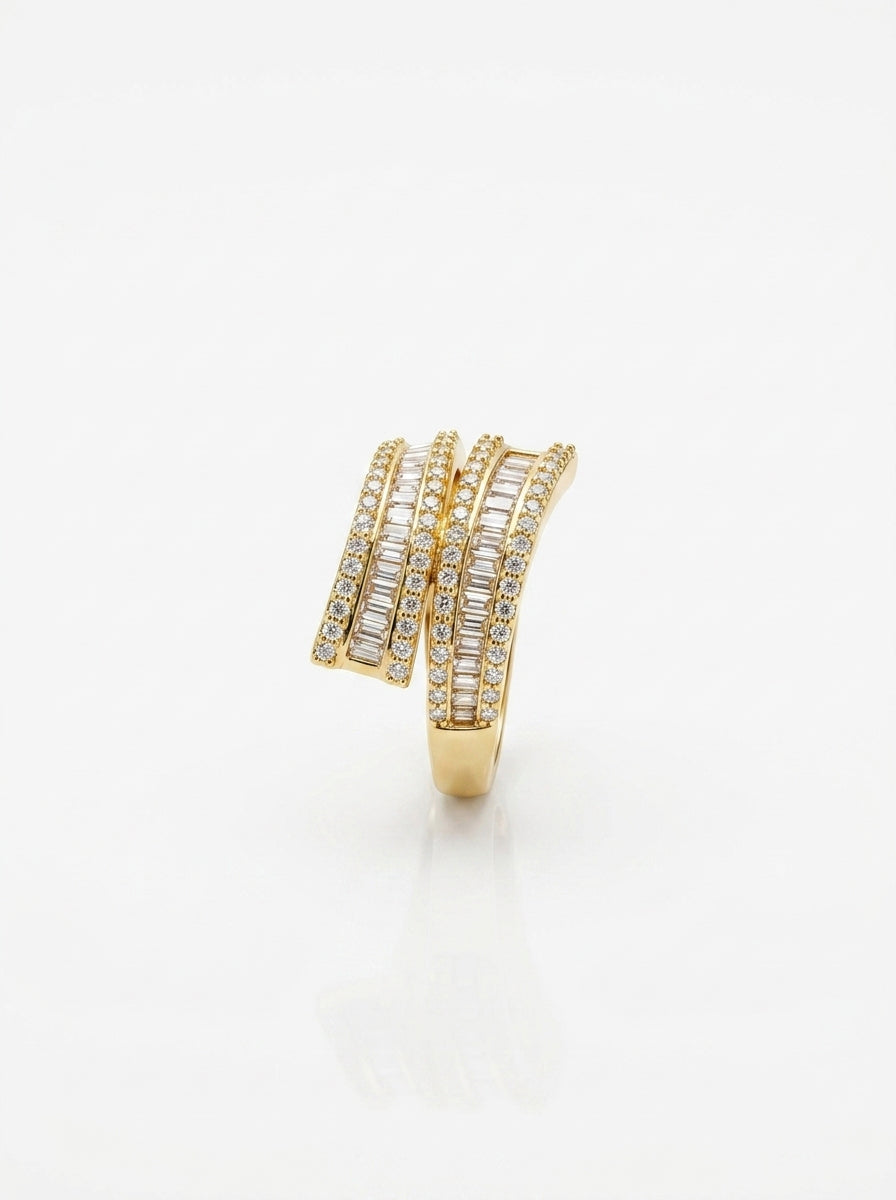 A gold wrap-style ring adorned with multiple rows of clear baguette and round-cut stones, photographed on a clean white background with a soft reflection below.