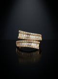 A pair of gold rings set with baguette-cut clear stones, displayed on a reflective black surface against a dark background.