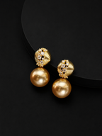 A pair of gold drop earrings with textured, diamond-like studs and large round gold pearls, displayed on a black background.