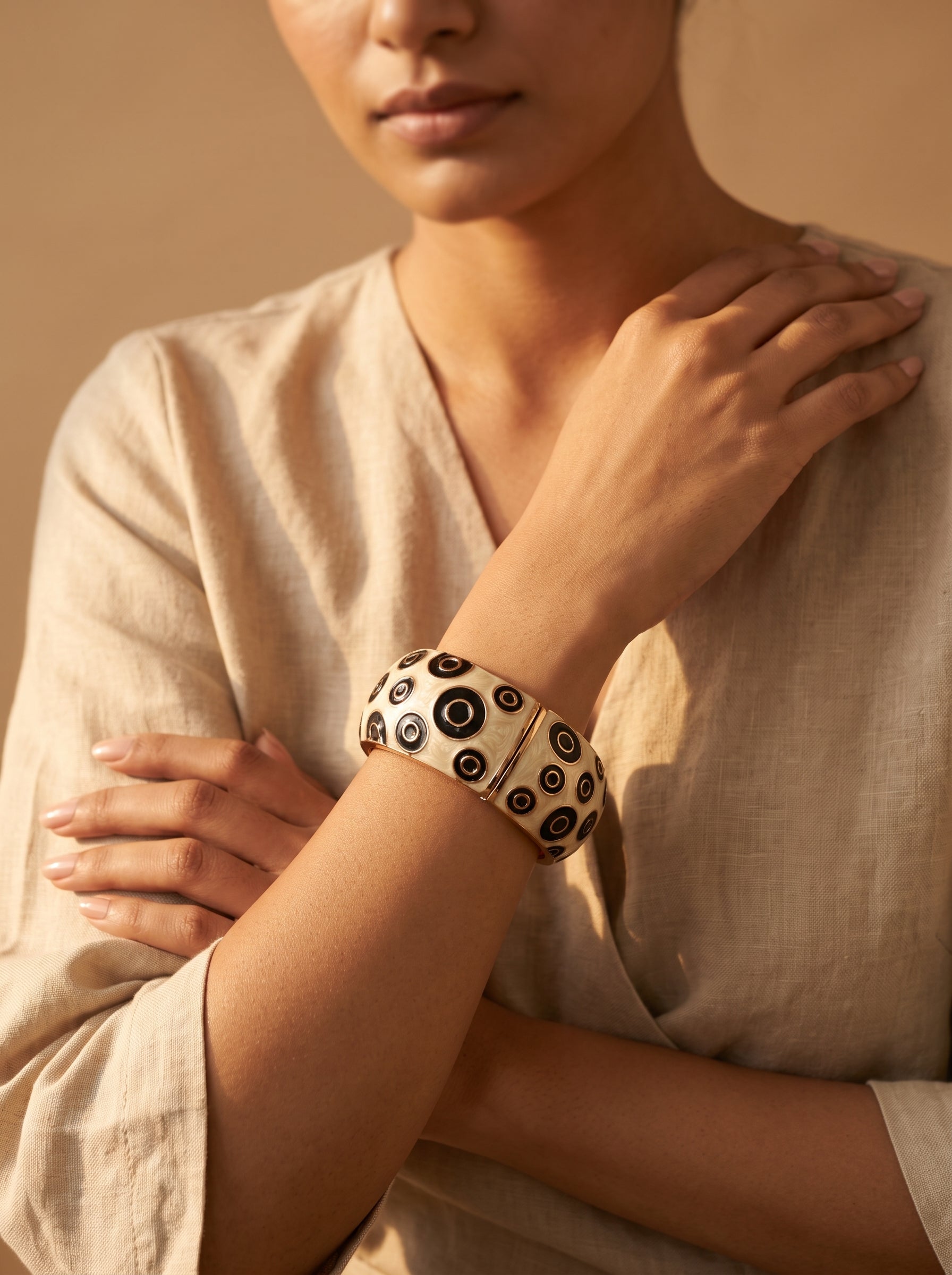 A close-up lifestyle shot of a model wearing a wide, flexible cuff bracelet. The bracelet is made of a cream-colored material with a pattern of black and dark brown concentric circles.