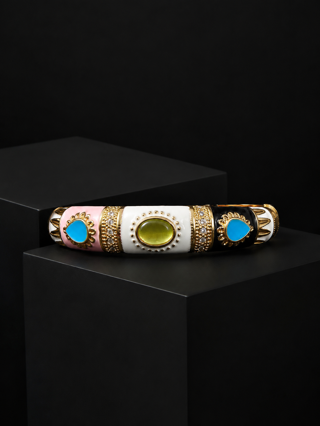 A decorative cylindrical bracelet or bangle displayed horizontally on a black pedestal. The bracelet has three main color sections: light pink, white, and black, separated by ornate gold filigree borders.