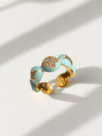 A gold-plated open cuff ring decorated with light blue enamel segments and small clear rhinestones, photographed on a white surface with soft diagonal shadows.