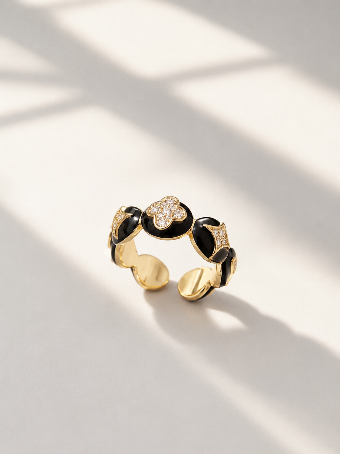 A gold and black enamel open ring with floral details, photographed on a light surface with soft window shadows.