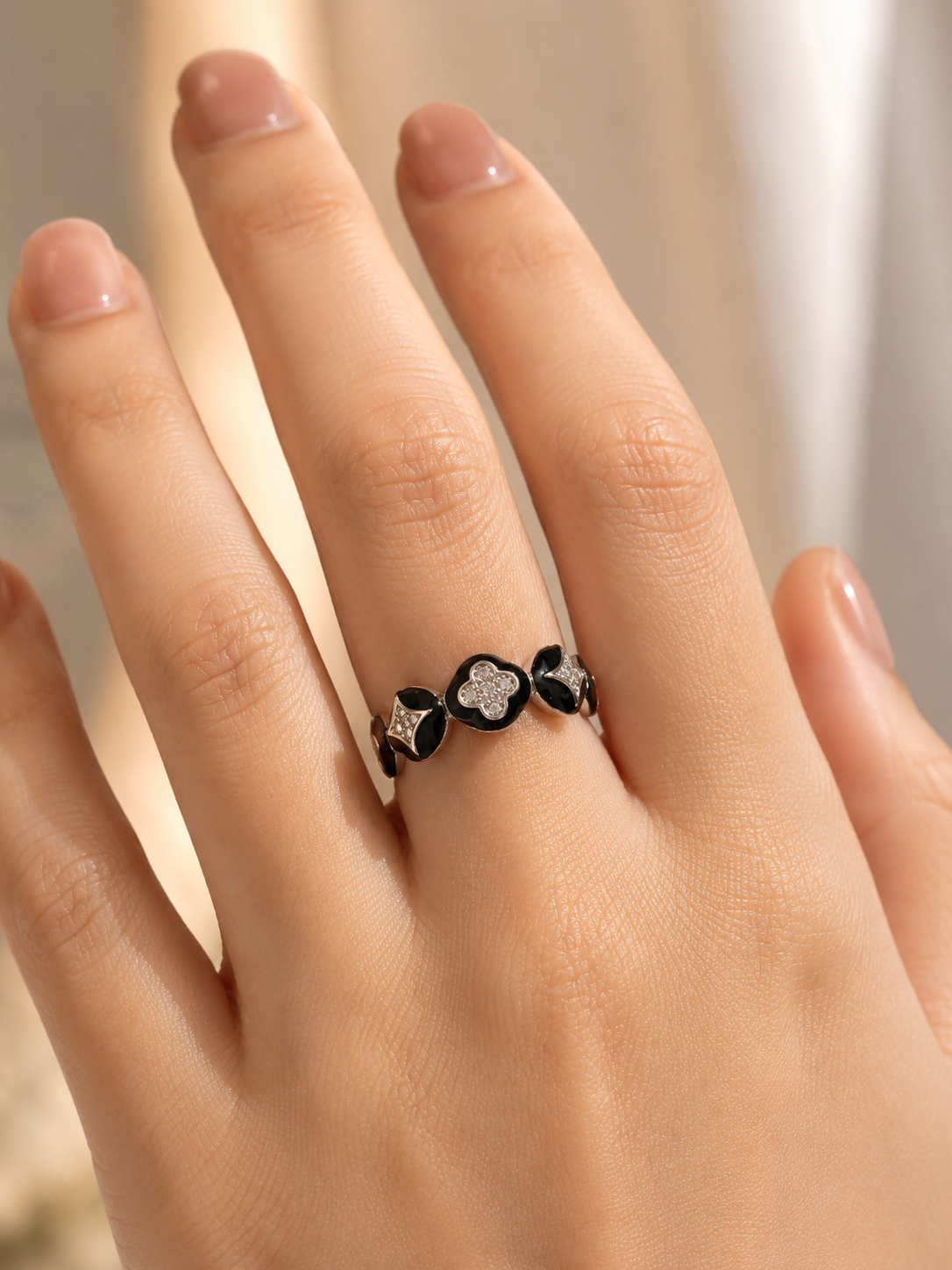 A close-up of a hand wearing a silver ring with three black clover-like motifs, each accented with small clear stones.