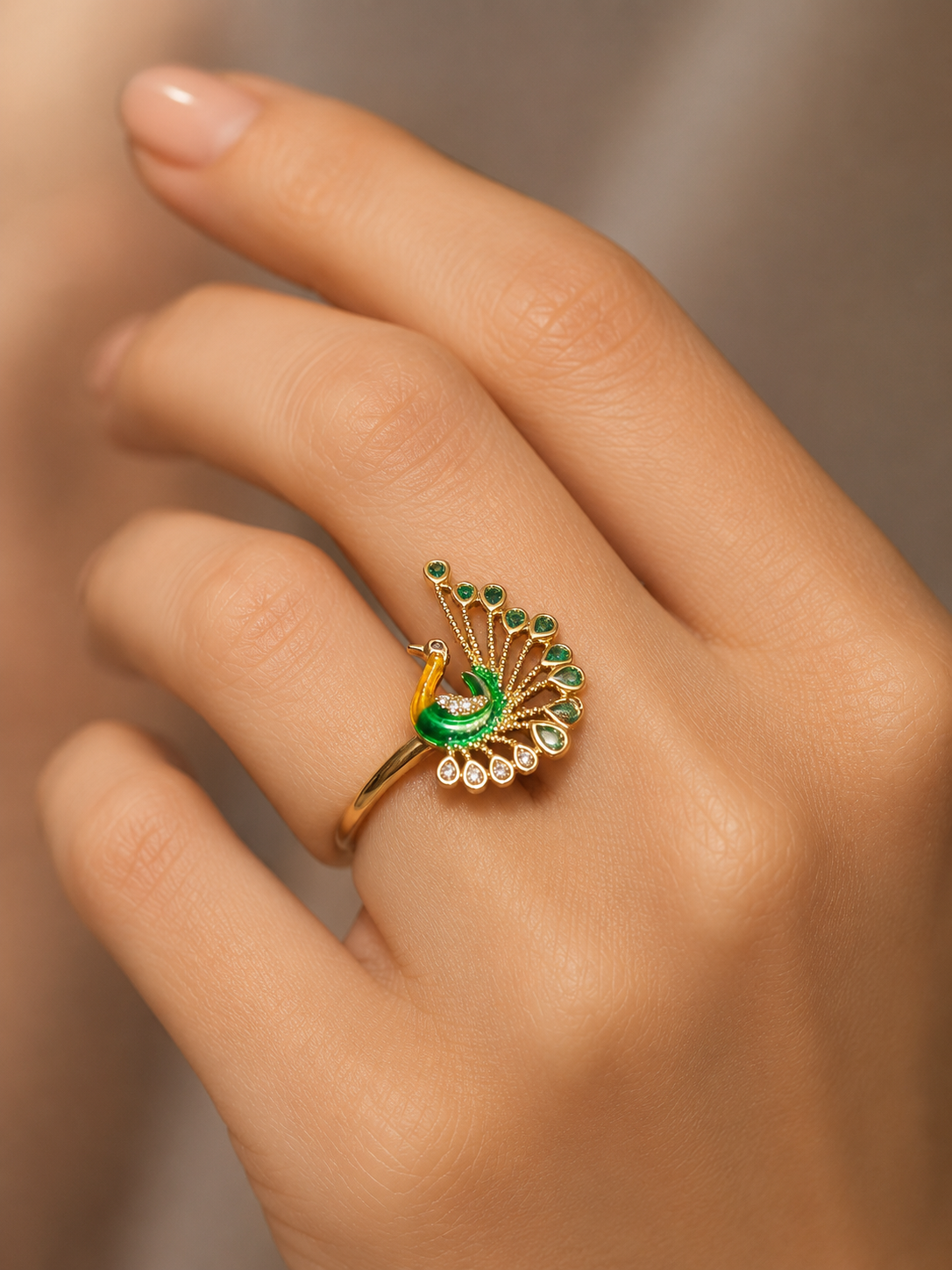 A gold ring designed like a peacock with green enamel and green gemstone accents, worn on a person's finger.