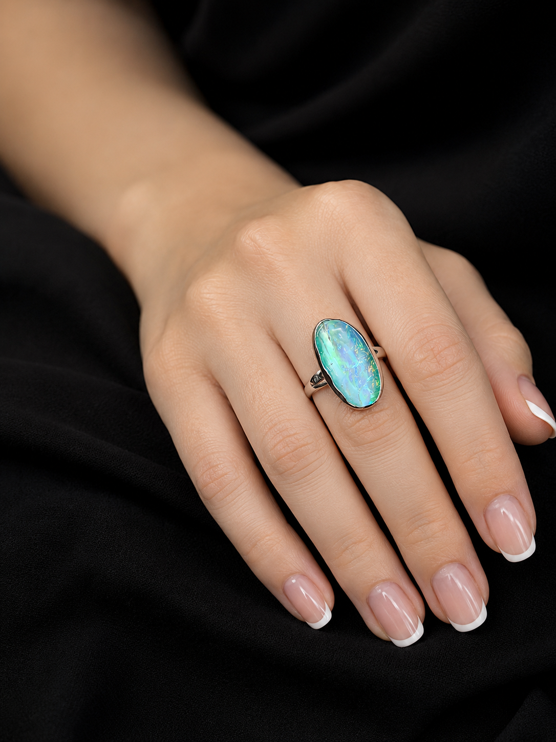 A close-up of a hand wearing a silver ring with a large oval turquoise-blue stone, set against a black background.