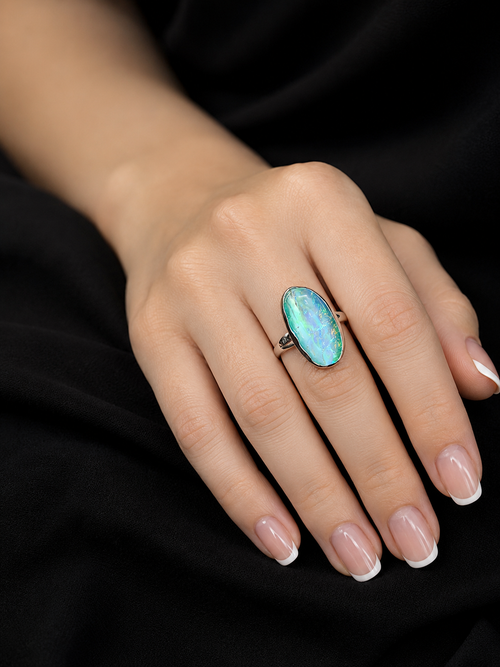 A close-up of a hand wearing a silver ring with a large oval turquoise-blue stone, set against a black background.