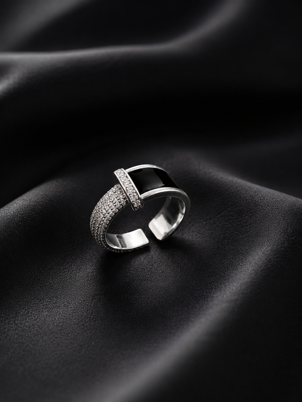 A silver-toned open band ring with a polished central bar and pavé-set stones, displayed on draped black fabric.