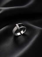 A silver-toned open band ring with a polished central bar and pavé-set stones, displayed on draped black fabric.
