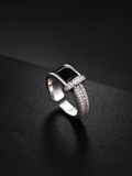 A silver-toned geometric ring with a rectangular black inlay and pavé-set clear stones, photographed on a dark textured surface.