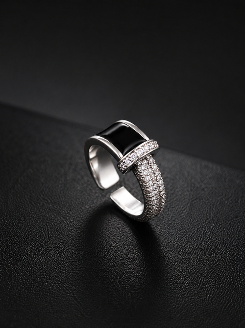 A silver-toned geometric ring with a rectangular black inlay and pavé-set clear stones, photographed on a dark textured surface.