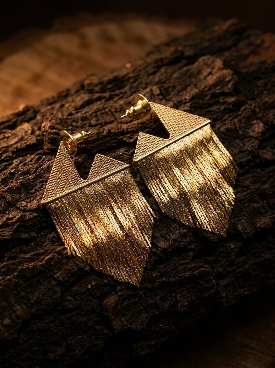 A pair of gold-toned geometric fringe earrings resting on a textured piece of dark wood bark.